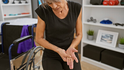 A mature woman examines her hand in a rehabilitation clinic, displaying recovery and healthcare...