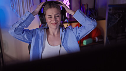 A beautiful young woman wearing a headset smiles with closed eyes in a colorful gaming room at night.