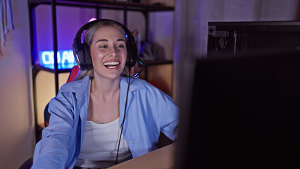 A joyful caucasian woman gaming indoors at night wearing headphones in a dark room with neon lights.