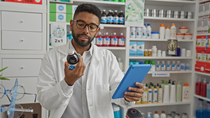 Handsome african american male pharmacist analyzing a medicine bottle while holding a digital...