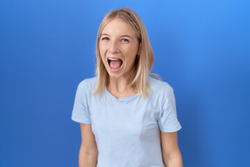 Young caucasian woman wearing casual blue t shirt angry and mad screaming frustrated and furious,...