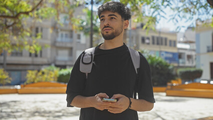 Handsome young man with beard using smartphone in sunlit city park