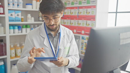 A bearded man working attentively on a tablet inside a modern pharmacy surrounded by shelves of...