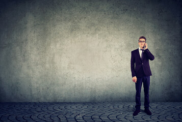 Obraz premium Business man standing by the wall and talking on cellphone 