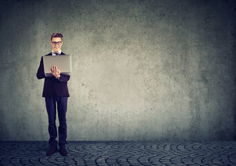 Happy business man with laptop computer standing by the wall 