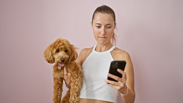 Young caucasian woman with dog smiling hugging using smartphone over isolated pink background