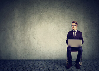 Happy businessman sitting on a chair with laptop computer looking to the side 