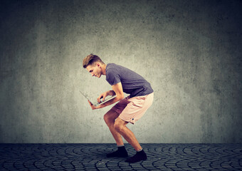 Young man using laptop while squatting along the wall