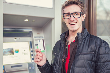Happy young man with debit card standing at ATM