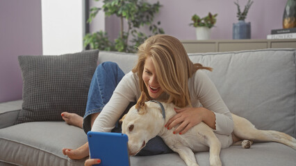 A young woman takes a selfie with her dog on a couch inside a cozy apartment.