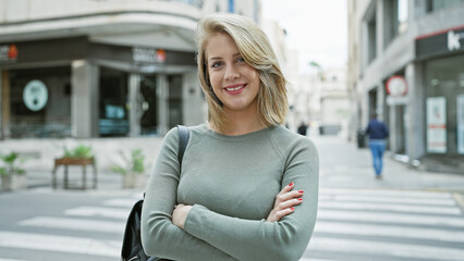Portrait of a confident young adult caucasian woman with short blonde hair, crossing arms on a city...
