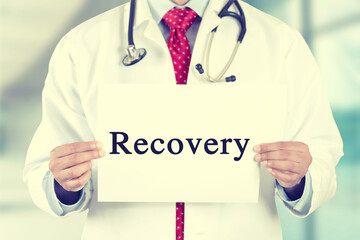 Closeup of doctor hands holding white card with recovery text message isolated on hospital clinic office background.