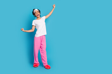 Full body portrait of pretty young woman stretching empty space wear pajama isolated on blue color...