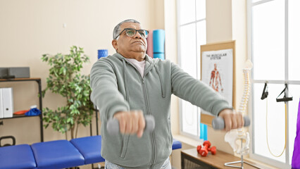 A mature man exercises with dumbbells in a bright physiotherapy rehabilitation center.