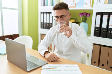 Obraz premium Young hispanic man business worker using laptop drinking water at office