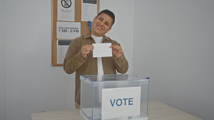 A smiling hispanic man casting a ballot in a voting booth during an election.
