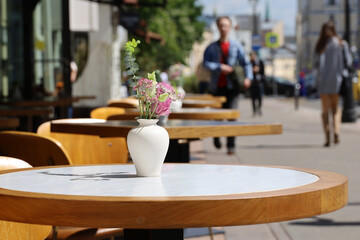 Street cafe in city with empty tables outdoor. Vases of flowers on round tables and cozy chairs in sunny day