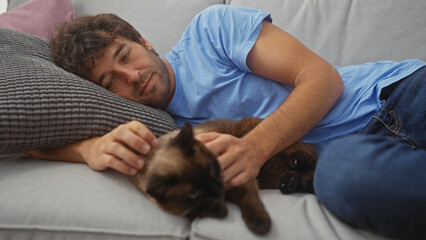 Young hispanic man relaxing on couch with his pet siamese cat in a cozy home interior.