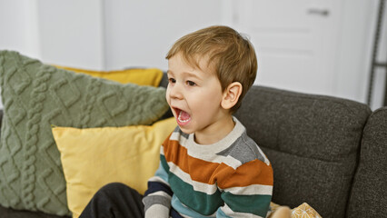 Young caucasian boy yelling while sitting on a gray sofa in a cozy living room setting