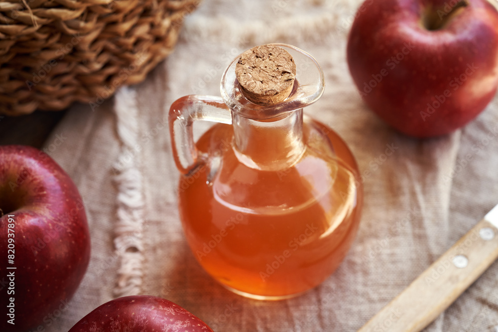 Wall mural A transparent glass jug of apple cider vinegar with fresh red apples