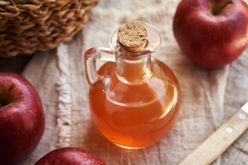 A transparent glass jug of apple cider vinegar with fresh red apples