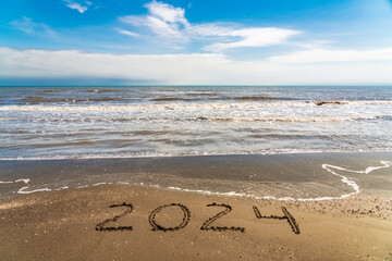 Hand written 2024 on wet sand is summer vacation theme background