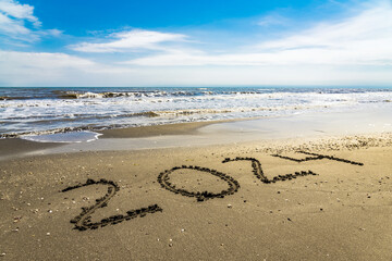 Hand written 2024 on wet sand is summer vacation theme background