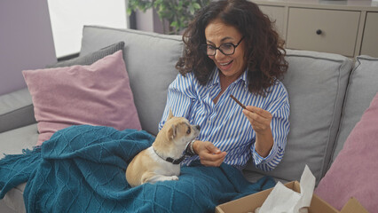 A middle-aged woman enjoys a playful moment with her chihuahua on a cozy sofa in a modern living...