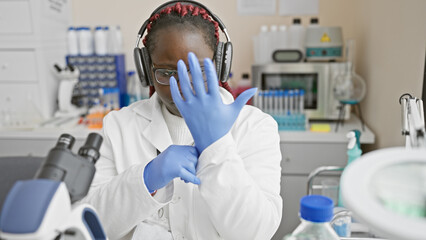 African woman scientist wearing headphones and blue gloves in a laboratory setting.