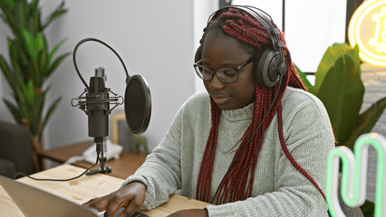 African american woman with braids using a microphone in a studio, wearing headphones