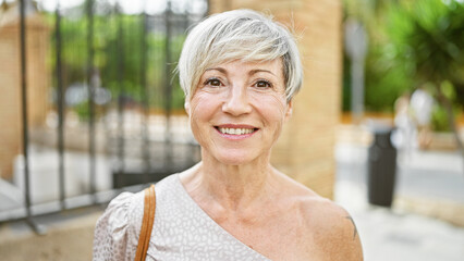Mature hispanic woman with short grey hair and a beautiful smile standing on a city street.