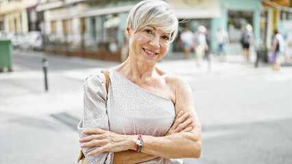 Mature hispanic woman with grey hair and crossed arms standing on a city street.