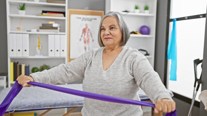 A senior woman exercises with a resistance band indoors at a rehabilitation center, showcasing...