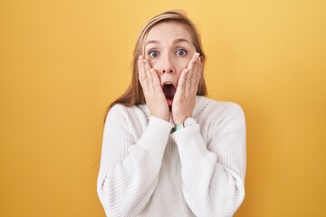 Young caucasian woman wearing white sweater over yellow background afraid and shocked, surprise and...