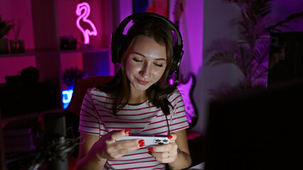 A young woman with headphones enjoys gaming in a neon-lit room at night.