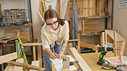 A young woman in safety glasses takes notes in a well-equipped carpentry workshop.