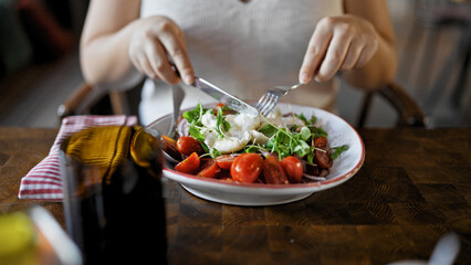 Young beautiful hispanic woman cutting salad at the restaurant