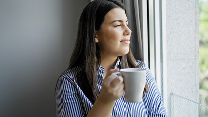 Young beautiful hispanic woman smiling looking through the window at home