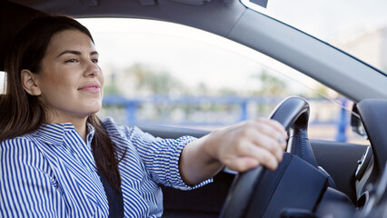 Young beautiful hispanic woman driving a car smiling on the road