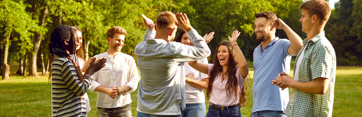 Group of a happy young people having fun giving each other high five while walking in the summer...
