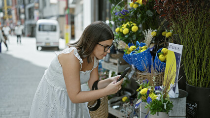 Beautiful hispanic woman in glasses snapping pictures of vibrant flowers on tokyo's streets