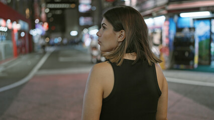 Beautiful hispanic woman disappears into tokyo's night, walking away on the city streets, leaving a view of her back in the cityscape under city lights