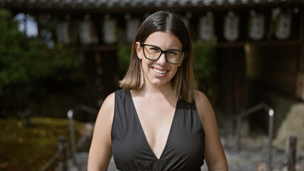Cheerful beautiful hispanic woman, proudly posing with her glasses on, flashing a gorgeous smile at kyoto's serene kodaiji temple