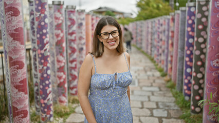 Fototapeta premium Cheerful hispanic woman in glasses poses with joy, smiling radiantly in kyoto's famous kimono forest, radiating pure happiness and casual confidence in a beautiful adult portrait.
