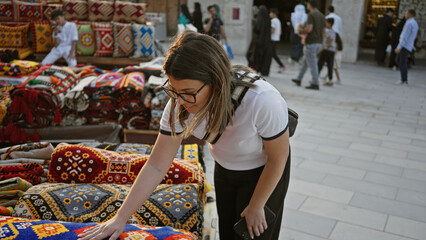 A young adult brunette woman examines colorful textiles at souq waqif marketplace in doha, qatar.