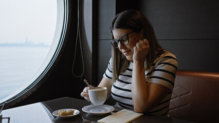 A contemplative young woman enjoys coffee by a porthole with a sea view on a cruise.