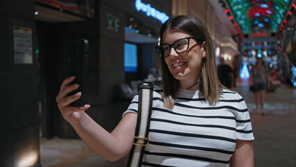 Smiling young latina woman with glasses takes a selfie aboard a luxurious modern cruise ship.