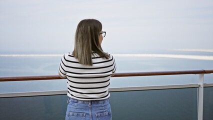 Back view of a contemplative young woman gazing over the sea on a cruise ship deck.