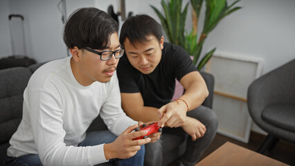 Two asian men enjoying a video game together in a cozy living room, exemplifying friendship and leisure.
