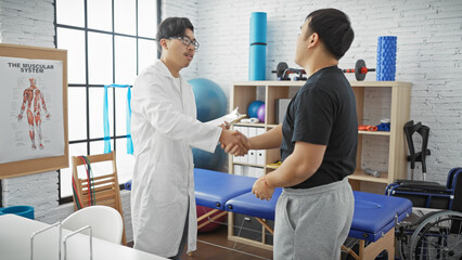 Obraz premium A male doctor and patient shaking hands in a physiotherapy clinic with rehabilitation equipment in the background.